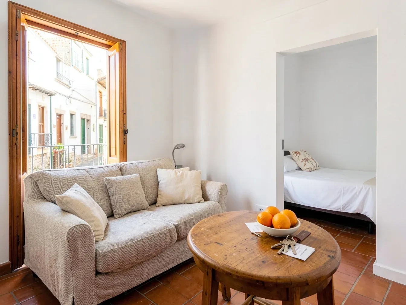 Salón luminoso de un apartamento turístico en el casco antiguo de Cádiz, con las llaves sobre la mesa y la cama hecha al fondo, listo para el siguiente huésped