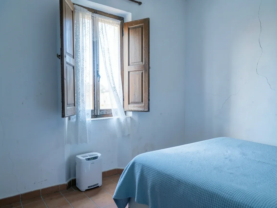 Bedroom in an old-town flat in Cádiz being aired with the window open and a dehumidifier running