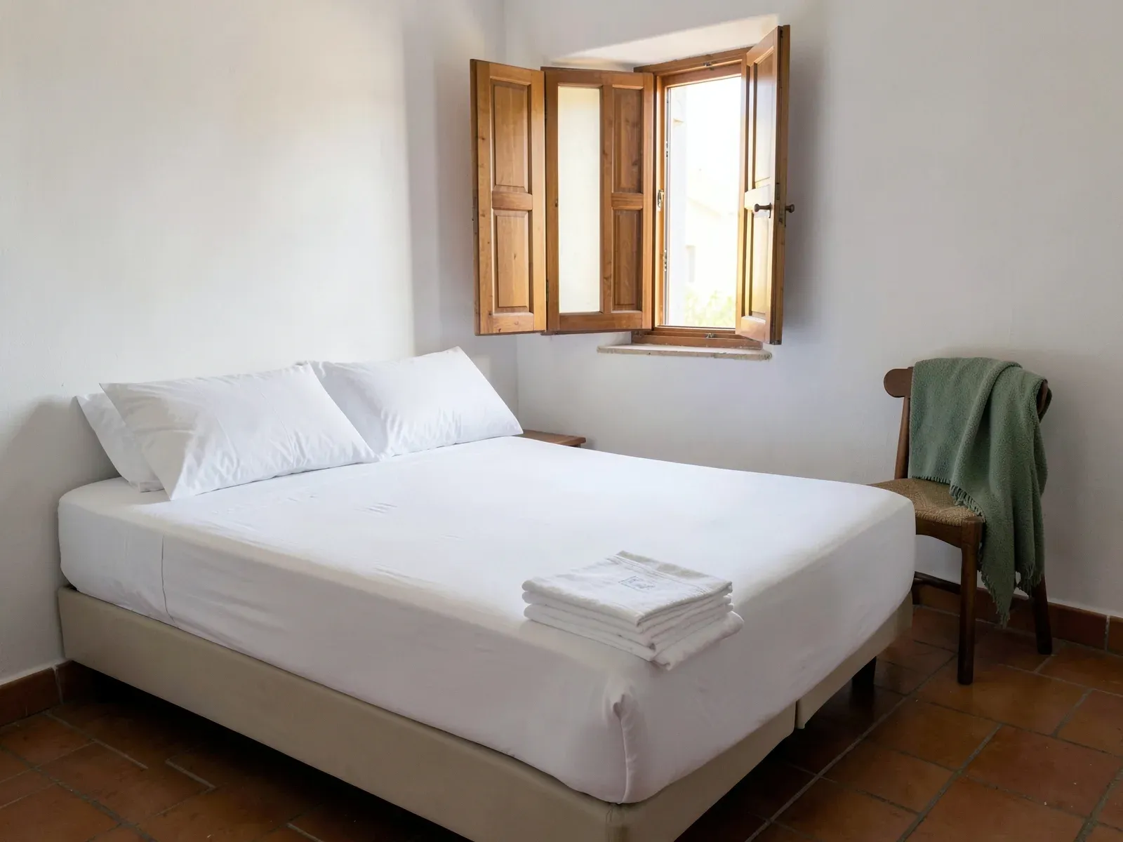 Dormitorio de un piso turístico durante la limpieza entre huéspedes, con la cama a medio hacer y una pila de sábanas y toallas limpias dobladas a los pies